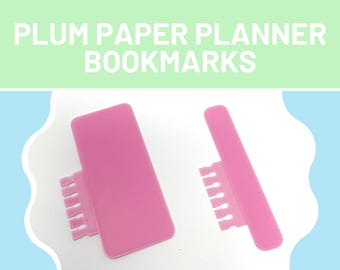 May include: Two pink bookmarks with a rectangular design and a notched edge. The text "PLUM PAPER PLANNER BOOKMARKS" is displayed in white letters on a green background, with a light blue background.