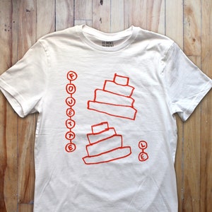 Op de afbeelding: Wit T-shirt met een rood grafisch ontwerp van twee gestapelde taarten en het woord "FOJETTE" verticaal geschreven aan de linkerkant van het shirt. De tekst "LES  BONES" en "OH  DANNY" staat gedrukt op het label.