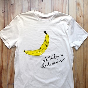 May include: White t-shirt featuring a yellow banana illustration and the text "Le Velours Souterrain" in black.