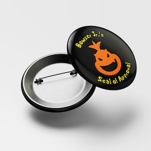 May include: A black button with a yellow and orange cartoon character with the text "Bowser Jr.'s Seal of Approval" on it.