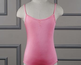 May include: A pink ballet leotard with thin spaghetti straps. The leotard is displayed on a mannequin. The fabric has a slight sheen. The background is a neutral gray with decorative molding.