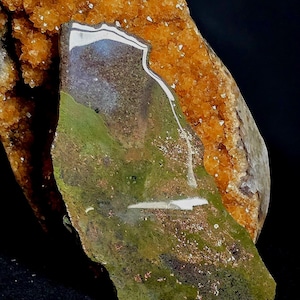 May include: A green, brown, and white iridescent stone with a rough, irregular shape. The stone is partially covered by a cluster of orange crystals.