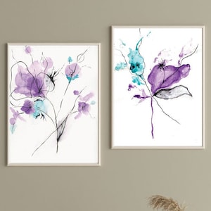 May include: Two framed watercolor floral art prints. The artwork features abstract purple and teal flowers with black line details on a white background. The frames are a light neutral color.