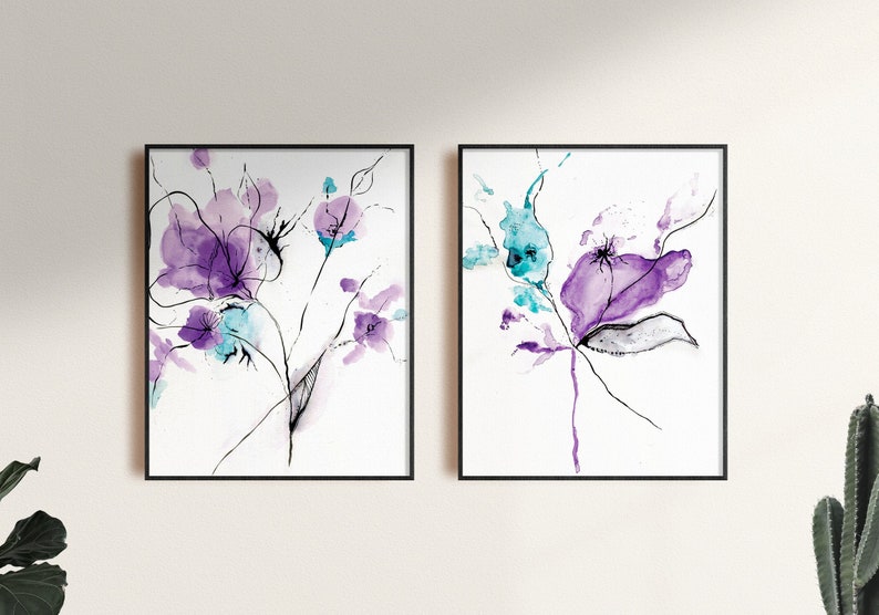 May include: Two framed floral art prints. Each print features watercolor flowers in shades of purple and teal, with delicate black line details. The artwork is set against a white background, creating a modern and elegant aesthetic.