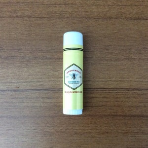 May include: A white tube of surfboard wax with a yellow label featuring a bee and the text "Honeybear Surfboard Wax, Southern California, HoneybearSurf.com".