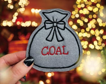 May include: A gray felt Christmas stocking with a black outline and a red bow. The stocking says "COAL" in red embroidery.