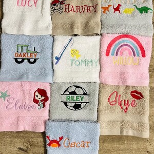 May include: Ten personalised towels with embroidered names and designs. The towels are in various colours, including pink, blue, beige, and white. The designs include a sunflower, a pirate skull, dinosaurs, a tractor, a fishing rod, a rainbow, a mermaid, a football, a kiss, and a crab.