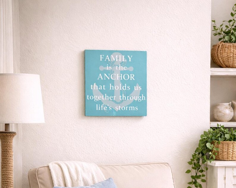 Coastal wood sign with painted in the Gulf with gray anchor design and quote “family is the anchor that holds us together through life’s storms,” displayed above a cozy armchair in a beach-style living room nook with soft neutral decor.
