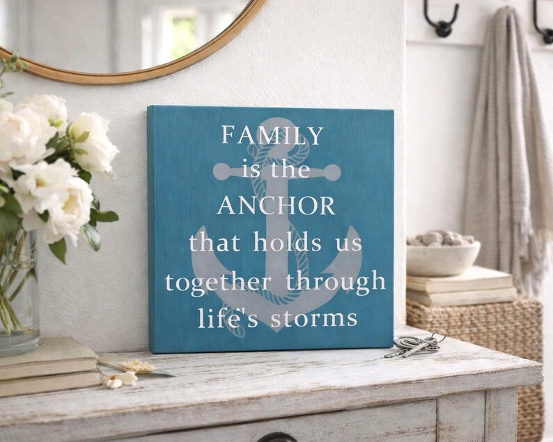 Turquoise coastal wood sign with gray anchor and white lettering reading “family is the anchor that holds us together through life’s storms,” displayed on a distressed white entryway table with flowers, books, and decorative accents.