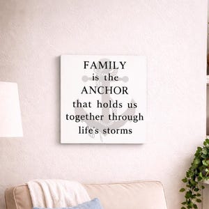White coastal wood sign with gray anchor and black lettering reading “family is the anchor that holds us together through life’s storms,” displayed above a beige armchair in a cozy beach-style living room nook.