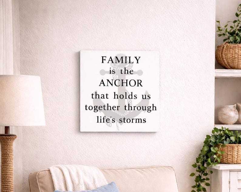 White coastal wood sign with gray anchor and black lettering reading “family is the anchor that holds us together through life’s storms,” displayed above a beige armchair in a cozy beach-style living room nook.