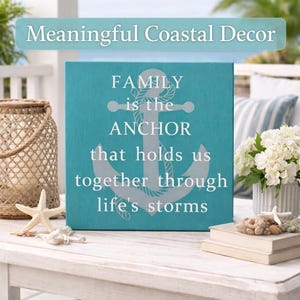 Turquoise coastal wood sign with anchor design and quote “family is the anchor that holds us together through life’s storms,” displayed on a beach-style porch table with seashells, lantern, and white hydrangeas.