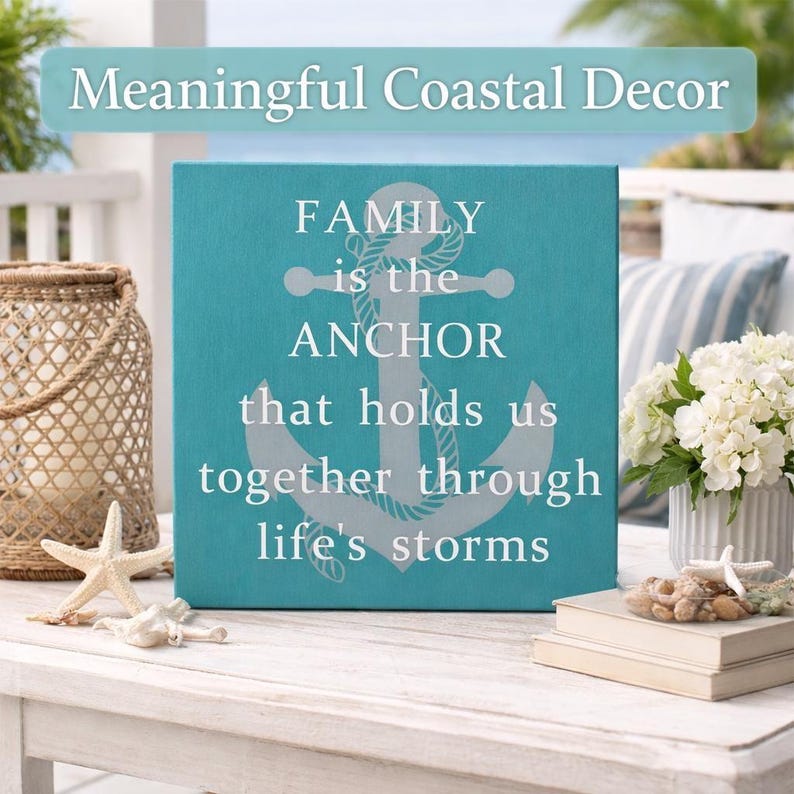 Turquoise coastal wood sign with anchor design and quote “family is the anchor that holds us together through life’s storms,” displayed on a beach-style porch table with seashells, lantern, and white hydrangeas.