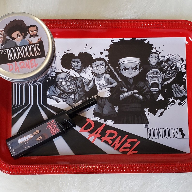 K&ouml;nnte beinhalten: Ein rotes Tablett mit einem schwarz-wei&szlig;en Grafikdruck mit Charakteren aus "The Boondocks" und dem Namen "Darnel" in Rot. Enth&auml;lt eine passende Dose und ein schwarzes Feuerzeug.