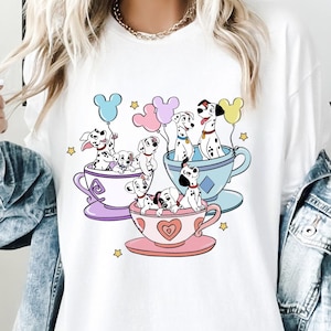 Può includere: Maglietta bianca con una grafica colorata di cuccioli dalmata in tazze da tè con palloncini. I cuccioli indossano collari rossi e le tazze da tè sono decorate con cuori e fiori.