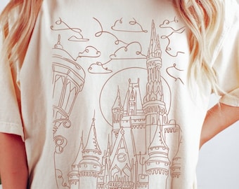 Peut inclure: Un t-shirt blanc avec un dessin au trait marron d'un château avec une lune et des nuages en arrière-plan.