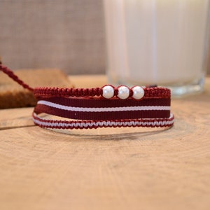 May include: A red, white and grey braided bracelet with three white pearl beads.