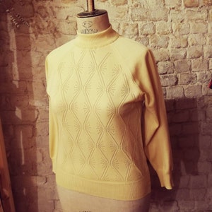 Op de afbeelding: Een lichtgele trui met een geometrisch patroon en een hoge hals. De trui heeft lange mouwen en een losse pasvorm.