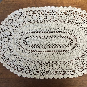 May include: A white crocheted oval doily with a delicate lace pattern.