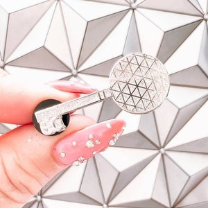 May include: Silver key-shaped pin with a sparkly finish. The key features a round, sparkly, silver charm in the shape of the Spaceship Earth at Epcot.