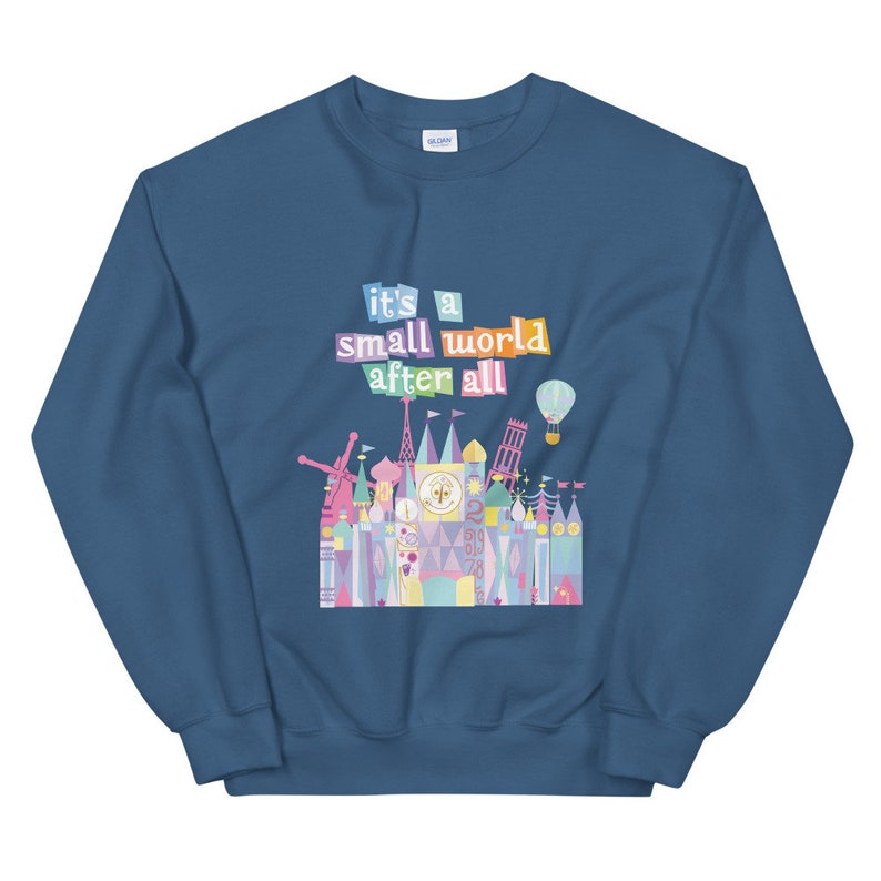 May include: A blue sweatshirt featuring the text "it's a small world after all" in colourful letters. The text is above a colourful illustration of the "it's a small world" ride at Disney World.