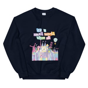 May include: Navy blue sweatshirt featuring a colourful graphic of the "it's a small world" ride at Disney World. The graphic includes the text "it's a small world after all".