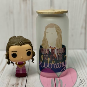 May include: A white frosted tumbler with a wooden lid and a straw. The tumbler has a graphic of a woman with the text "When in doubt go to the library".