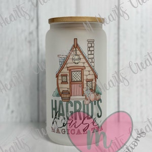 May include: White frosted glass jar with a gold lid. The jar has a graphic of a small house with a chimney and a lantern. The text "Hagrid's House Magical Tea" is printed on the jar.