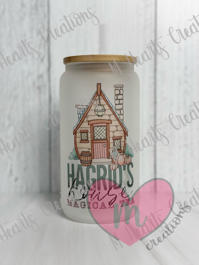 May include: White frosted glass jar with a gold lid. The jar has a graphic of a small house with a chimney and a lantern. The text "Hagrid's House Magical Tea" is printed on the jar.