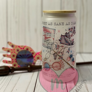 May include: White tumbler with a wood lid featuring a whimsical illustration of glasses, a cork necklace, a wand, and a magazine cover with the text "Quibbler". The text "Just as sane as I am" is printed on the tumbler.
