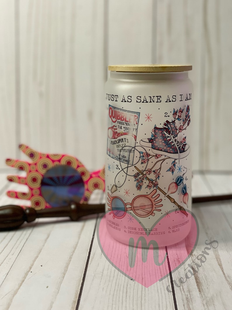 May include: White tumbler with a wood lid featuring a whimsical illustration of glasses, a cork necklace, a wand, and a magazine cover with the text "Quibbler". The text "Just as sane as I am" is printed on the tumbler.