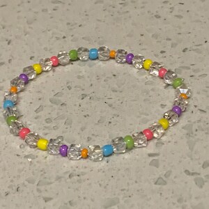 May include: A colorful beaded bracelet with clear, round beads and small, colorful beads in shades of pink, yellow, green, blue, and purple.