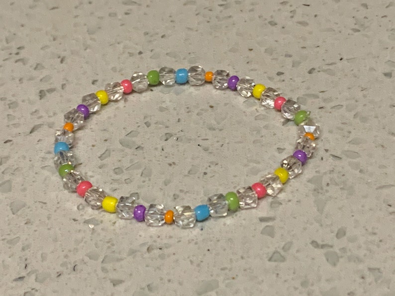 May include: A colorful beaded bracelet with clear, round beads and small, colorful beads in shades of pink, yellow, green, blue, and purple.