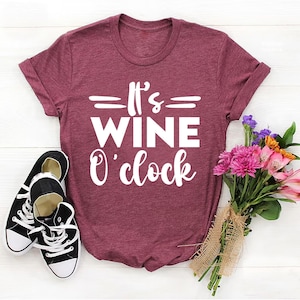 May include: A maroon t-shirt with the text "It's Wine O'clock" printed in white.