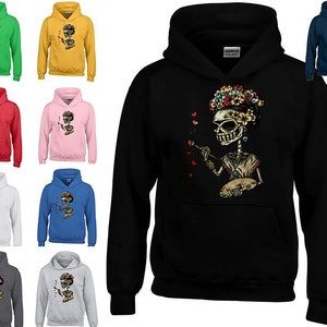 Peut inclure: Sweat-shirt à capuche noir avec une illustration colorée de crâne portant une couronne de fleurs et tenant un pinceau et une palette. Le crâne tient un pinceau et une palette. Le crâne porte une couronne de fleurs. Le crâne est entouré de cœurs rouges.