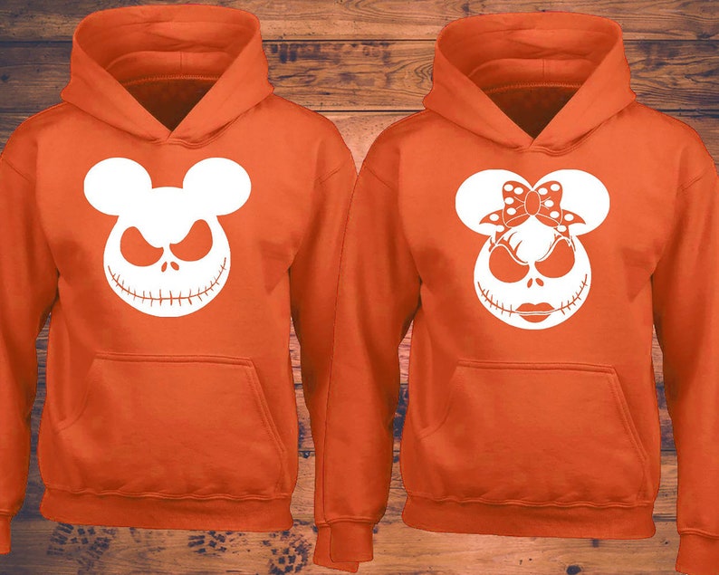 Puede incluir: Dos sudaderas con capucha de color naranja con dise&ntilde;os de Jack Skellington en blanco. Una sudadera con capucha presenta a Jack Skellington con orejas de Mickey Mouse, la otra presenta a Jack Skellington con orejas de Minnie Mouse y un lazo.