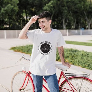 May include: A white t-shirt with a black graphic design featuring a circle with stars and the text "Five Billion Star Hotel".