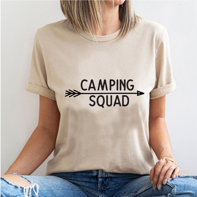 May include: A beige t-shirt with a black arrow and the text "Camping Squad" printed on the front.