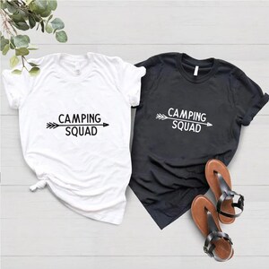 May include: Two t-shirts with the text "Camping Squad" and an arrow graphic. One shirt is white and the other is black.