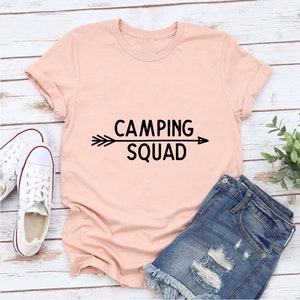 May include: A pink t-shirt with a black graphic that says "Camping Squad" with an arrow pointing to the right.