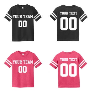 May include: Two pairs of black and pink youth football jerseys with white stripes on the sleeves. The jerseys have a white number "00" and the text "YOUR TEAM" or "YOUR TEXT" on the front.