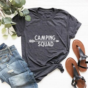May include: A dark gray t-shirt with a white arrow and the text "CAMPING SQUAD" printed on the front.