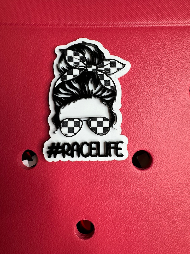 Op de afbeelding: Een witte sticker met een zwart-wit geruit patroonontwerp van een vrouw met een rommelige knot en zonnebril. De tekst "#RACELIFE" staat onder de afbeelding van de vrouw.