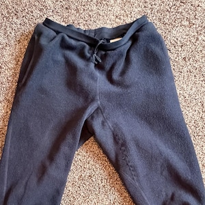 Peut inclure: Pantalon de survêtement en polaire bleu marine foncé avec taille élastique et poches. Le pantalon est fait d'une matière douce et moelleuse, idéal pour se détendre ou pour une tenue décontractée. Le pantalon est présenté sur un tapis marron.