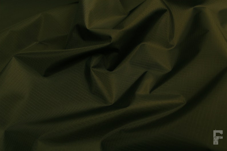 May include: A close-up of a dark green fabric with a subtle textured pattern. The fabric is wrinkled and folded, creating a soft, drapey look.