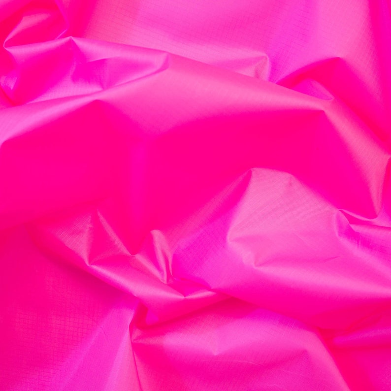 May include: A close-up of a bright pink fabric with a smooth, silky texture. The fabric is wrinkled and folded, creating a soft, flowing look.