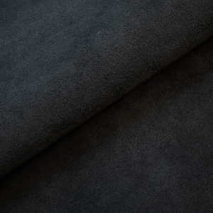 May include: Close-up of a dark gray suede fabric. The fabric is folded in half, showing the texture of the material.