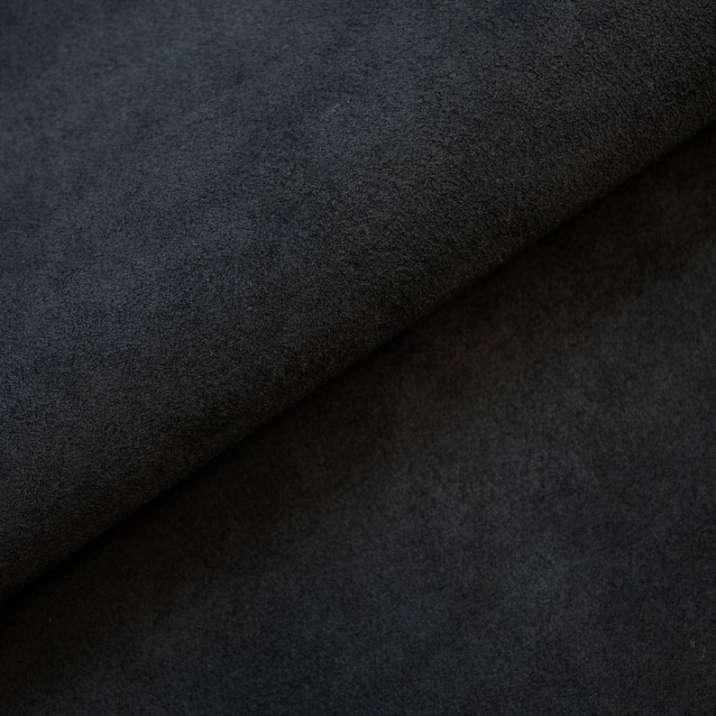 May include: Close-up of a dark gray suede fabric. The fabric is folded in half, showing the texture of the material.