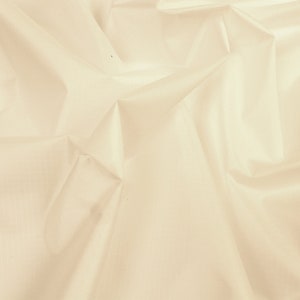 May include: A close-up of a smooth, off-white fabric with a subtle sheen. The fabric is draped and folded, creating soft, flowing lines.