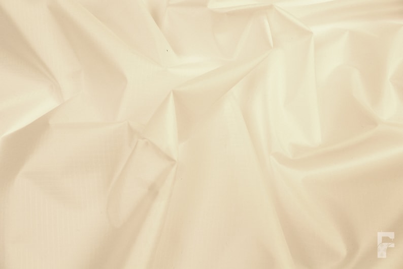 May include: A close-up of a smooth, off-white fabric with a subtle sheen. The fabric is draped and folded, creating soft, flowing lines.
